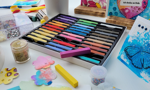 Kreativgarten Klangschalentherapie und kreative Malkurse in Rosenheim. Farbenfroher Kreativtisch mit Pinseln, Papier und bunten Werken – eine Einladung zum freien Gestalten im Kreativgarten von Mea Lumina.