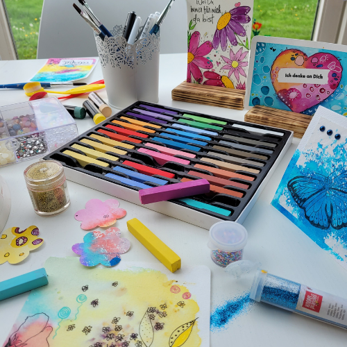 Kreativgarten Klangschalentherapie und kreative Malkurse in Rosenheim. Farbenfroher Kreativtisch mit Pinseln, Papier und bunten Werken – eine Einladung zum freien Gestalten im Kreativgarten von Mea Lumina.